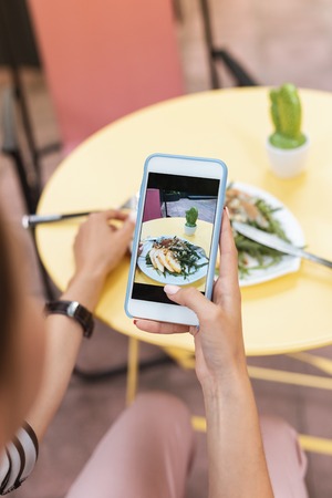 Woman wearing nice black leather watch making photo of her salad standing near cactus