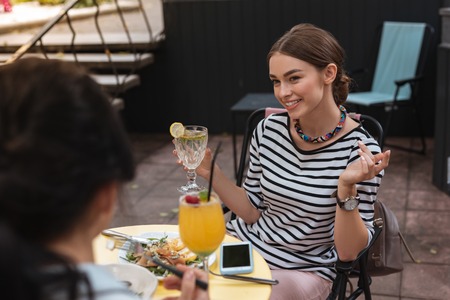 Happy fashionable woman having tasty dinner with her best friend in new restaurantの写真素材
