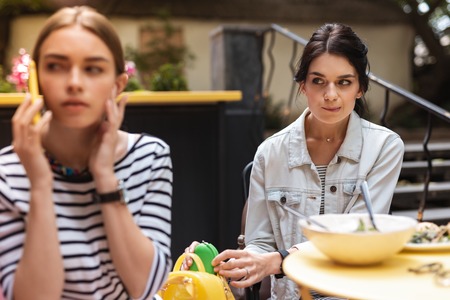 Without intention. Sly dark-haired friend taking cosmetics bag of her friend without her intentionの写真素材