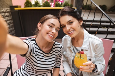 Woman with phone. Dark-haired woman wearing striped shirt holding phone while making photo with her friendの写真素材