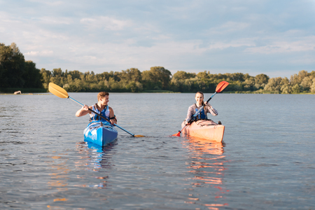 Lovely girlfriend. Active blonde-haired man looking at his lovely girlfriend while kayaking togetherの写真素材
