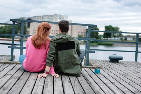 Romantic place. Joyful nice couple looking at the river while sitting together on the dockの写真素材