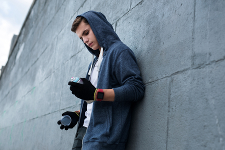 Serious young man standing near the wall while looking at the spray paintの写真素材