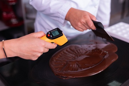 Chocolate temperature. Professional experienced chocolatier measuring chocolate temperature for glazeの写真素材