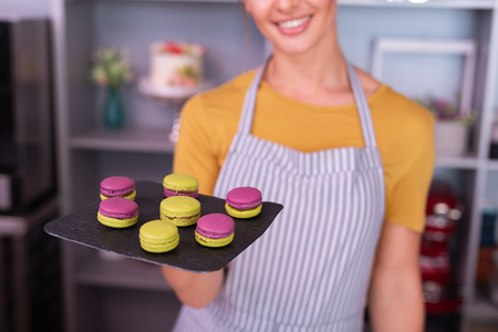 Smile after cooking. Young baker wearing striped apron smiling broadly after cooking bright macaroonsの写真素材