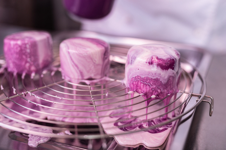 Cakes in trivet. Three little delicious sweet blueberry cakes with mirror icing on them standing on trivetの写真素材