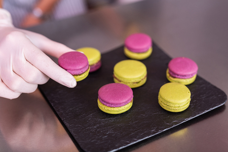 Holding macaroons. Professional confectioner wearing white gloves holding nice pink and yellow macaroonsの写真素材
