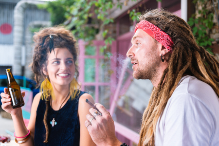 Cigar and beer. Stylish hippie man smoking cigar while his beautiful fashionable girlfriend drinking beerの写真素材