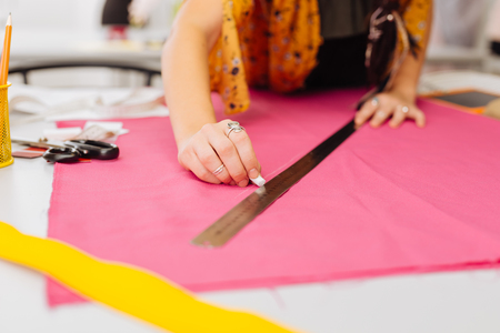 Holding chalk. Careful attentive dressmaker putting her hands on the pink fabric while being in the atelier and drawing the linesの写真素材
