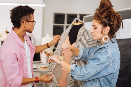 One pin. Serious female dressmaker standing near a young man and taking one pin from the pin cushion