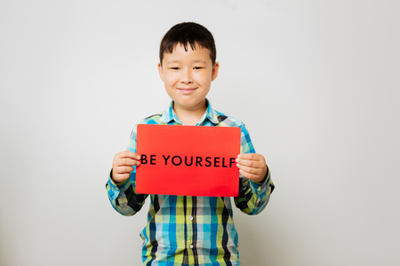 Against racism. Sweet Asian kid holding a table while standing in a roomの写真素材