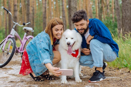 Making photo. Cute young couple stopping in the park for making photo with their white fluffy dog