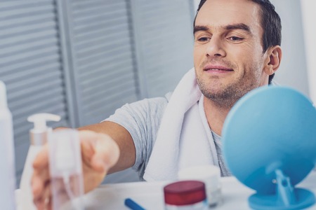 Skin care. Handsome pleasant looking man taking care of his skin while using face creamの写真素材