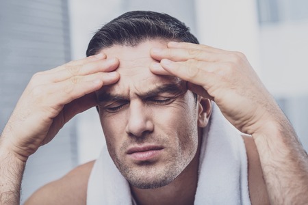 Strong headache. Close up of concentrated serious man keeping his eyes closed and touching his forehead with his hands while feeling tiredの写真素材