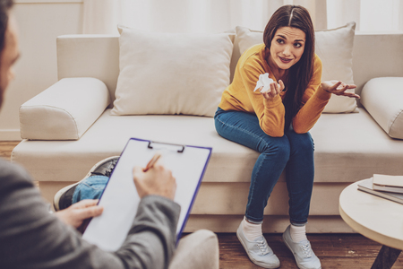 Professional help. Young female person wrinkling forehead while talking with her practitionerの写真素材