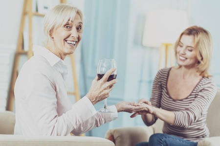 Cheerful aged woman drinking a glass of wine while celebrating the engagement of her daughterの写真素材