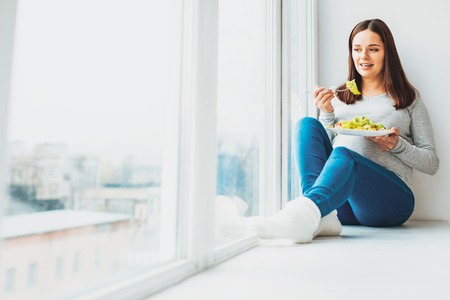 Warm socks. Pregnant cheerful woman sitting on window sill wearing warm socks feeling memorableの写真素材