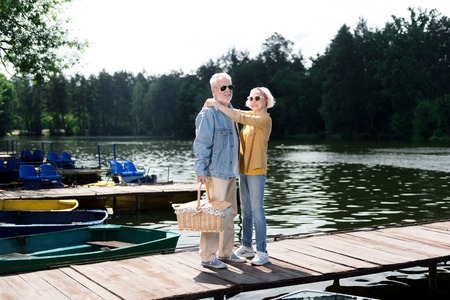 Stylish husband. Beaming aged woman feeling lovely while hugging her handsome stylish husband in jeans jacketの写真素材