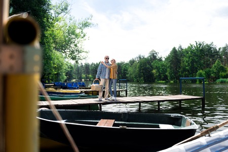 Standing on bridge. Couple of elderly wife and husband standing on the wooden bridge near little boatの写真素材