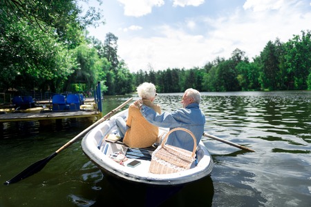 Picnic in boat. Elderly couple wearing fashionable clothes spending warm summer day having picnic in...