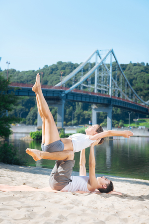 Stressless life. Loving positive man and woman trying yoga on beach and building mutual trustの写真素材