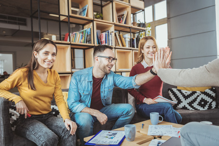 Nice job. Vigorous four colleagues exchanging high five and laughing