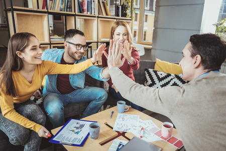 Jolly four colleagues exchanging high five and smiling