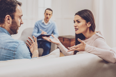 Family quarrel. Cheerless young woman talking to her husband while having a quarrel with him during the psychological sessionの写真素材