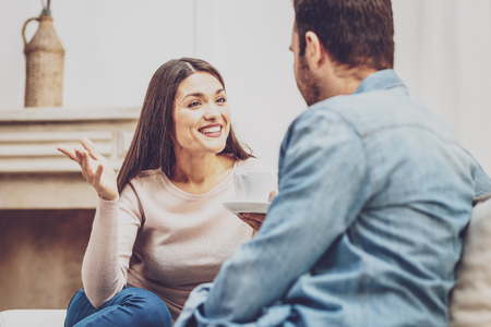 Positive mood. Joyful happy woman talking to her boyfriend while drinking coffee with himの写真素材
