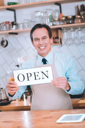 Cheerful smiling male standing at his workplace while demonstrating tabletの写真素材