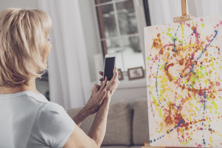 Picture of canvas. Blonde-haired elderly woman feeling motivated while taking picture of her creative colorful canvasの写真素材