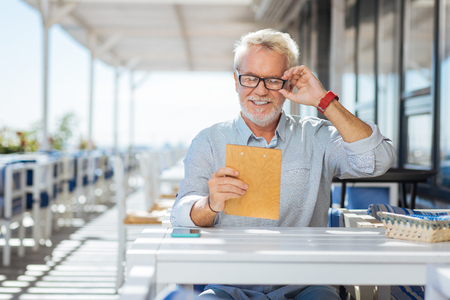 Eyesight problems. Happy cheerful man fixing his glasses while trying to read the menuの写真素材