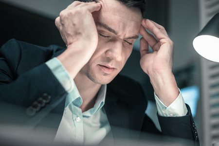 Headache. Hardworking business man feeling tired after hard day at work suffering from headacheの写真素材
