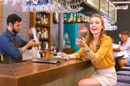 Sudden meeting. Cheerful young girl sitting at the bar counter and smiling while noticing her friendsの写真素材