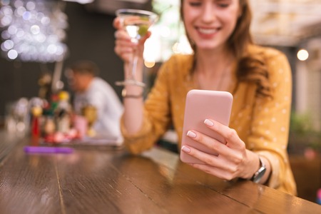 Holding smartphone. Beautiful young girl sitting in the bar and smiling while holding her smartphoneの写真素材