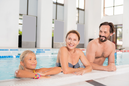 Healthy lifestyle. Joyful nice family smiling to you while visiting an indoor poolの写真素材