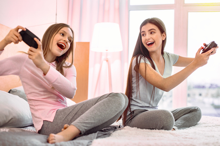 Keep smiling. Cheerful brunette female looking at her friend and playing video gameの写真素材