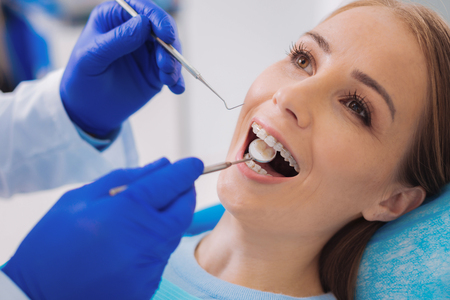 Opening mouth. Cheerful calm patient opening her mouth and a calm careful dentist looking at the teeth with a help of a dental mirrorの写真素材