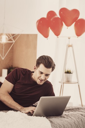 Family photos. Young husband feeling sentimental while watching family photos from summer vacation on silver laptopの写真素材