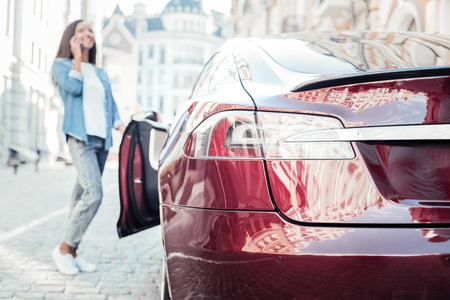 I have business. Silhouette of delighted girl that keeping smile on her face and talking per telephone while standing in semi position near carの写真素材