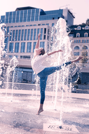 Beautiful fountain. Nice pleasant female dancer holding her leg up while being among the waterの写真素材