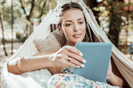 Day off. Nice young woman having a good time resting in park holding a tabletの写真素材