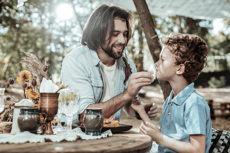 Supportive father. Pleasant bearded father washing his sons face finishing dinner in the gardenの写真素材