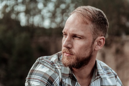 Handsome man. Close up of handsome bearded blonde-haired man feeling rather thoughtful and serious after changes in his lifeの写真素材