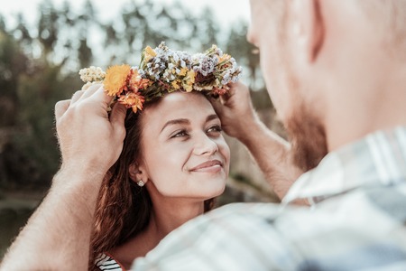 Appealing woman. Loving bearded man putting beautiful floral chaplet on head of his appealing beaming green-eyed womanの写真素材