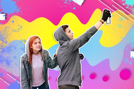 Painting quickly. Young vandal drawing on the wall with a help of spray paint and his girlfriend...