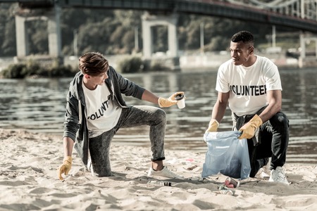 Classmates talking. Two classmates talking to each other while gathering empty coffee cups on the beach participating in voluntary workの写真素材