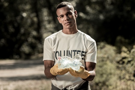 Active volunteer. Active volunteer wearing bright yellow gloves and white shirt with volunteer sign cleaning up the forestの写真素材
