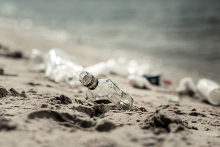 Alcohol bottle. Close up of big empty glass alcohol bottle laying on sand near the beautiful river...