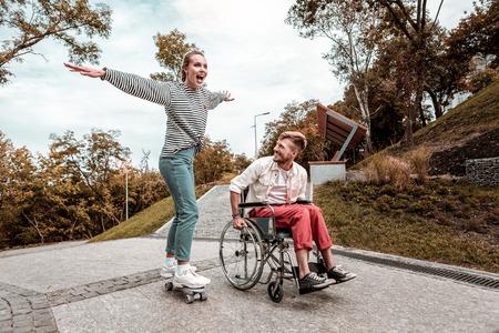 Happy with skateboard. Cheerful man smiling and enjoying spending time with his active girlfriend...